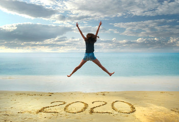 Obraz premium New Year 2020 on the sand,happy girl with hands up jumping on the beach