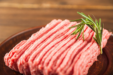 Ground chicken with a sprig of rosemary on a wooden plate on a textural table. Turkey mince raw close-up and copy space.