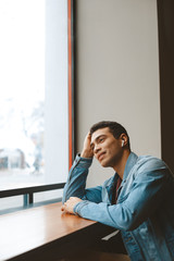 Handsome joyful guy sitting at the table and propping his head up with hand