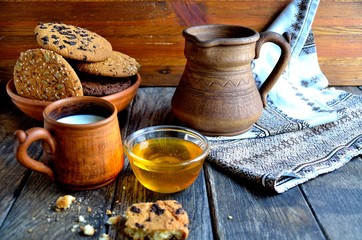 Oatmeal cookies in a ceramic rustic plate, milk in a ceramic mug, napkin, honey on a rustic wooden table.
