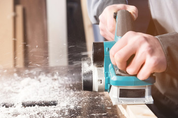 The hands of a carpenter working woodworking power tools. Close up of the work of the electric planer