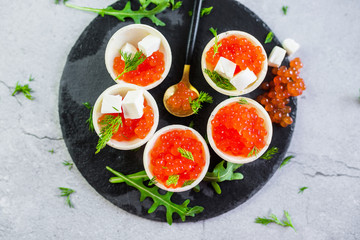 Red caviar on black plate with spoon and creamy cheese. Food photo concept