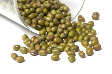 Closeup of mungo beans falling from glass container on white background