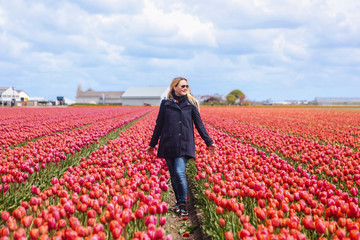 Dreamy beautiful long haired blond woman wearing blue coat standing in a field of pink tulips