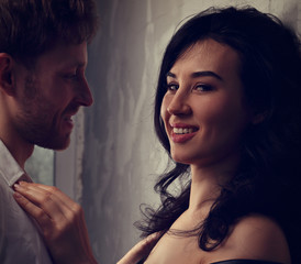 Sexy couple portrait. Man in white shirt looking on his sensual smiling beautiful girlfriend with much emotion in dark drama light with dark shadow.