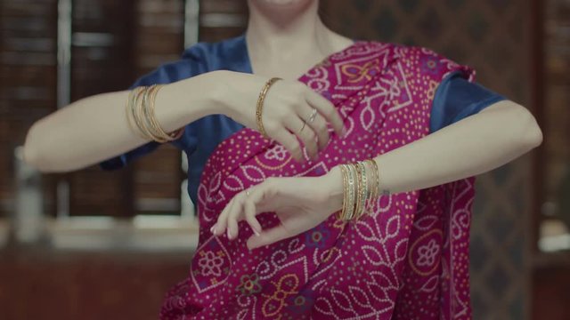 Midsection of graceful women in colorful sari with many precious bracelets performing ethnic hindu dance in oriental interior. Close-up of female hands making smooth dance moves while dancing.