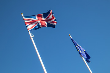 British Union Jack flag and European Union flag flying on flag poles against a blue sky