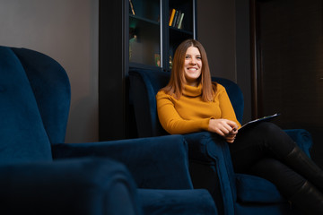 Image of smiling woman psychologist in yellow sweater sitting on blue chair.