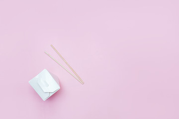 Opened takeaway box for chinese noodles presented with chopsticks, on pink background Retail set flatlay copyspace