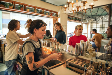 Naklejka premium Young female bartender pouring cocktails behind a bar counter