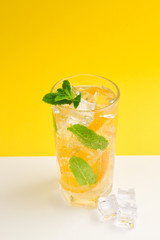 Cocktail with lemon and mint on a yellow background. Copy space.