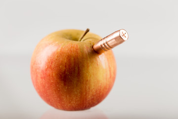 Copper bullet sticks out of a red apple on a gray background, shallow depth of field.