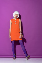 Full length view of stylish young woman in white wig standing on purple background