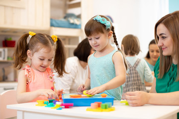 Group of kids with teacher playing with developmental toys in kindergarten