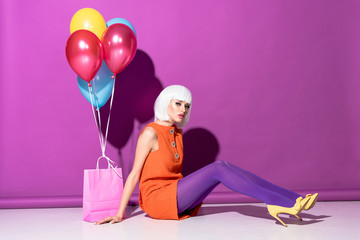 Charming young woman in wig with air balloons sitting on purple background