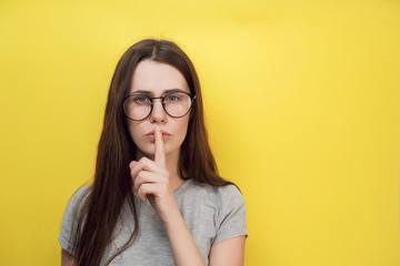 Beautiful surprised young female with shocked expression demonstrates silence gesture, keeps fore...