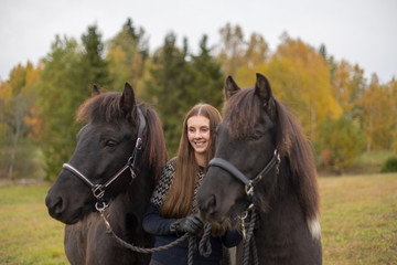 Smiling young swedish woman with her two black Icelandic horses