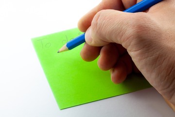Hand writes "to do list" with blue pencil on green note paper, isolated on white background