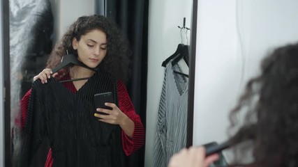 Woman is trying dresses in changing room in shop and taking selfie by mobile