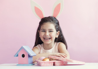 Happy little child wearing bunny ears on Easter day. Girl holding painted eggs.