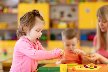 Nurdery babies playing with play clay in kindergarten or playschool