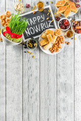 Happy Nowruz holiday background. Celebrating Nowruz sweets and treats- baklava, various dried fruits,  nuts, seeds, wooden background with green grass, copy space