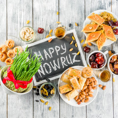Happy Nowruz holiday background. Celebrating Nowruz sweets and treats- baklava, various dried fruits,  nuts, seeds, wooden background with green grass, copy space