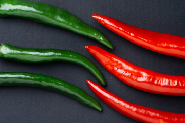 Green and red chili peppers on black background, top view. Hot spicy food symbol.