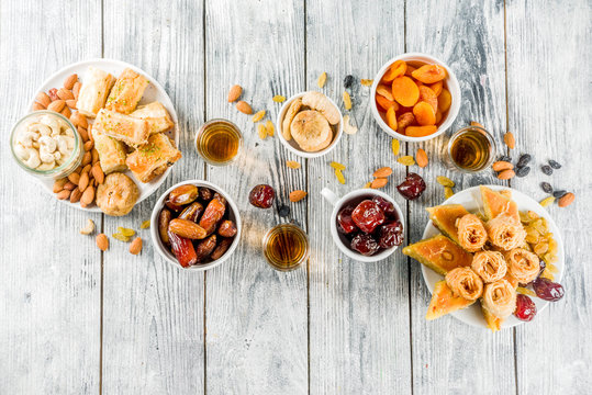 Set various Middle Eastern Arabian sweets - Turkish baklava, knafeh (kunaf), nuts, dried fruits and seeds. White wooden background, top view copy space