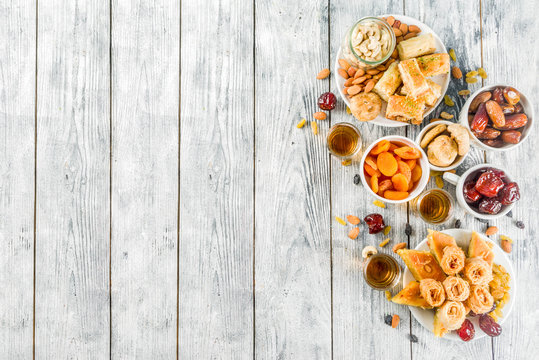 Set various Middle Eastern Arabian sweets - Turkish baklava, knafeh (kunaf), nuts, dried fruits and seeds. White wooden background, top view copy space