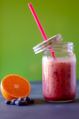 Glass jar with straw of pink smoothie surrounded by blueberries and half orange