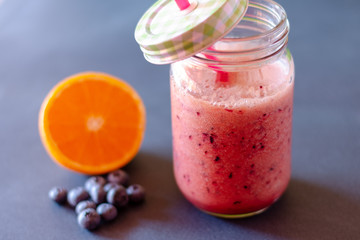 Jar with straw of pink smoothie surrounded by blueberries and half orange