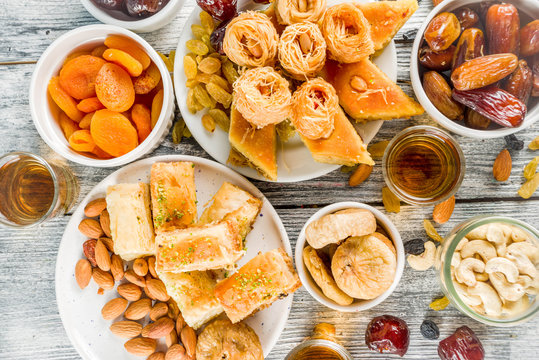 Set various Middle Eastern Arabian sweets - Turkish baklava, knafeh (kunaf), nuts, dried fruits and seeds. White wooden background, top view copy space