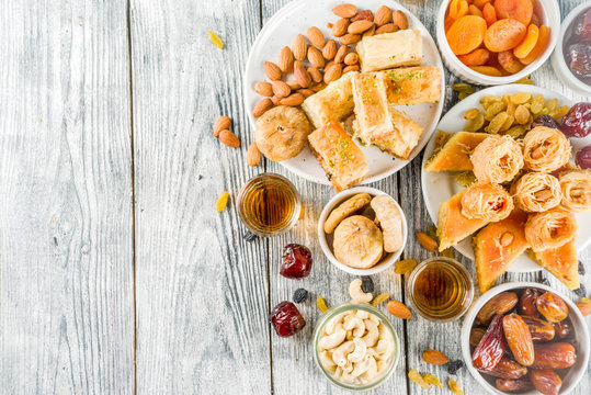 Set various Middle Eastern Arabian sweets - Turkish baklava, knafeh (kunaf), nuts, dried fruits and seeds. White wooden background, top view copy space
