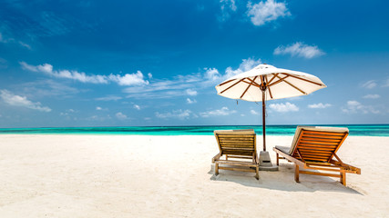 Romantic beach scene, two lounge chairs and umbrella on white sand. Honeymoon or vacation concept, couple and luxury travel background