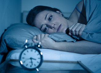 Attractive woman in bed staring at alarm clock trying to sleep feeling stressed and sleepless