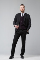 Elegant man in a three-piece suit stands in full growth on a gray background.
