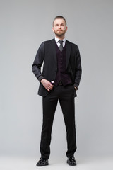 Elegant man in a three-piece suit stands in full growth on a gray background.