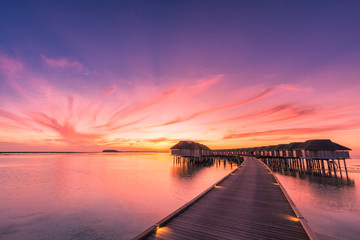 Sunset on Maldives island, luxury water villas resort and wooden pier. Beautiful sky and clouds and...