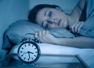 Attractive woman in bed staring at alarm clock trying to sleep feeling stressed and sleepless