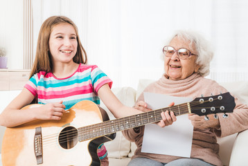 Smiling granddaughter playing on guitar for grandmother