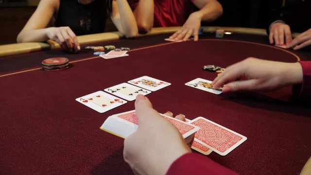 Casino dealer putting cards on red table, poker game, gambling, close-up hands. Players on background.