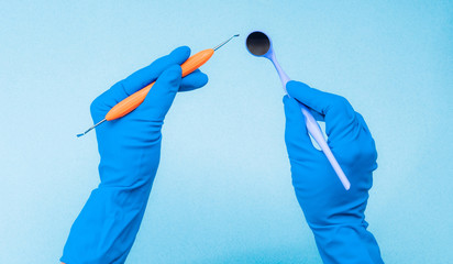 Hands in blue gloves holding dental instruments on light blue background