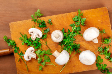 Champignon mushrooms, whole and sliced, shot from the top on a rustic cutting board with fresh parsley leaves and a place for text