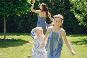 Naklejka na ściany i meble beautiful long-haired mother in a long blue dress in sunny summer forest walks with his beautiful daughters