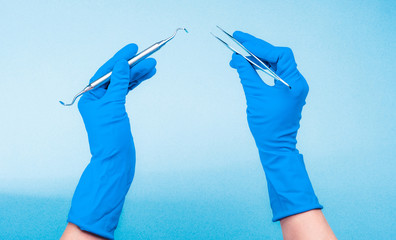 Hands in blue gloves holding dental tools on light blue background