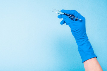 Hand in blue glove holding dental tweezers on light blue background - obrazy, fototapety, plakaty