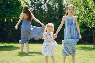 Naklejka premium beautiful long-haired mother in a long blue dress in sunny summer forest walks with his beautiful daughters