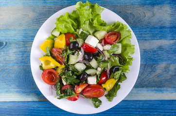 Vegetable salad cucumber capsicum tomato and olives on a white plate genuine blue background copy space