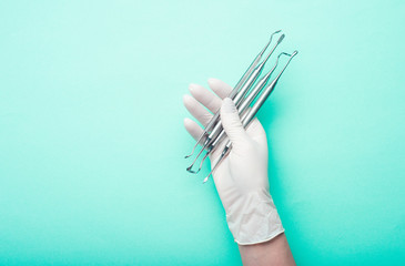 Hand in glove holding dental tools on light turquoise background
